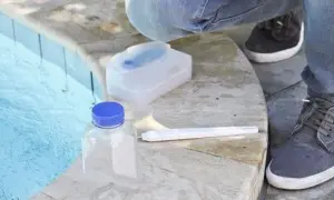 Test de piscine : une bouteille, un kit et une personne vérifient s'il y a trop de sel dans la piscine.