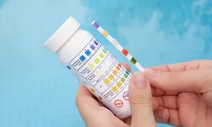 Bandelette test pour piscine, comparant la couleur des carrés à un tableau pour vérifier le pH et le chlore.