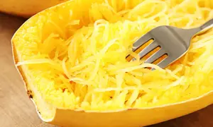 Une fourchette décompose les fils jaunes d'une courgette spaghetti cuite, prête à être dégustée.