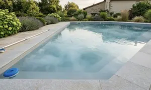 Piscine propre et prête pour la baignade après chlore choc. Un balai et un diffuseur de chlore flottent à la surface.