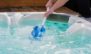 Nettoyage d'un spa en hiver avec un aspirateur manuel. L'eau est turquoise et des bulles se forment.