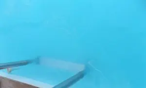 Nettoyage d'une piscine : un aspirateur sous-marin racle le fond, soulevant une eau trouble. Le sel dissous rend l'eau légèrement laiteuse.