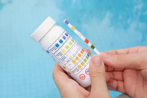 Bandelette test pour piscine, comparant la couleur des carrés à un tableau pour vérifier le pH et le chlore.