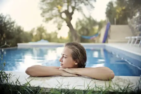 Jeune femme aux cheveux mouillés, profitant d'un moment de détente au bord de la piscine. L'eau bleue reflète le ciel, créant une ambiance paisible.