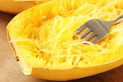 Une fourchette décompose les fils jaunes d'une courgette spaghetti cuite, prête à être dégustée.