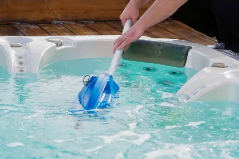 Nettoyage d'un spa en hiver avec un aspirateur manuel. L'eau est turquoise et des bulles se forment.