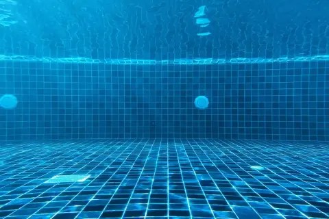 Vue sous-marine d'une piscine carrelée de bleu. La lumière du soleil filtre à travers l'eau. Question : chlore choc combien de temps faire tourner la pompe ?