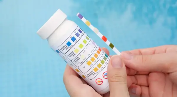 Bandelette test pour piscine, comparant la couleur des carrés à un tableau pour vérifier le pH et le chlore.