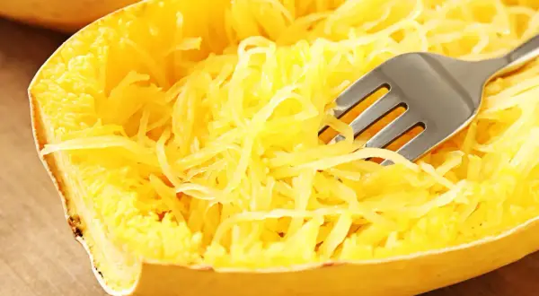 Une fourchette décompose les fils jaunes d'une courgette spaghetti cuite, prête à être dégustée.