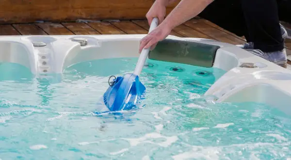 Nettoyage d'un spa en hiver avec un aspirateur manuel. L'eau est turquoise et des bulles se forment.