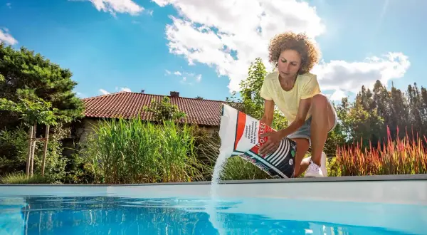 Femme versant du sel dans une piscine, assurant le bon temps de dissolution du sel pour une eau cristalline.