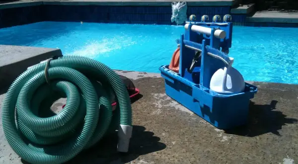 Kit d'entretien piscine pour les nuls : tuyau vert enroulé et boîte bleue avec accessoires de nettoyage.