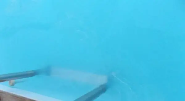 Nettoyage d'une piscine : un aspirateur sous-marin racle le fond, soulevant une eau trouble. Le sel dissous rend l'eau légèrement laiteuse.