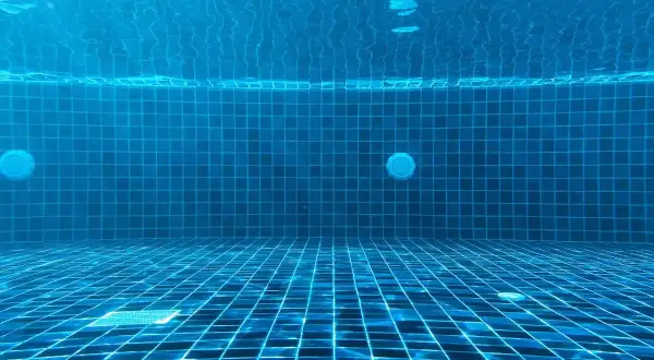 Vue sous-marine d'une piscine carrelée de bleu. La lumière du soleil filtre à travers l'eau. Question : chlore choc combien de temps faire tourner la pompe ?