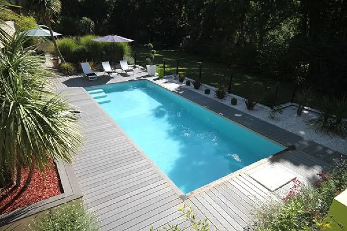 Piscine avec terrasse en bois, transats et parasols. Le **dosage sel piscine** est essentiel pour une eau claire et saine.