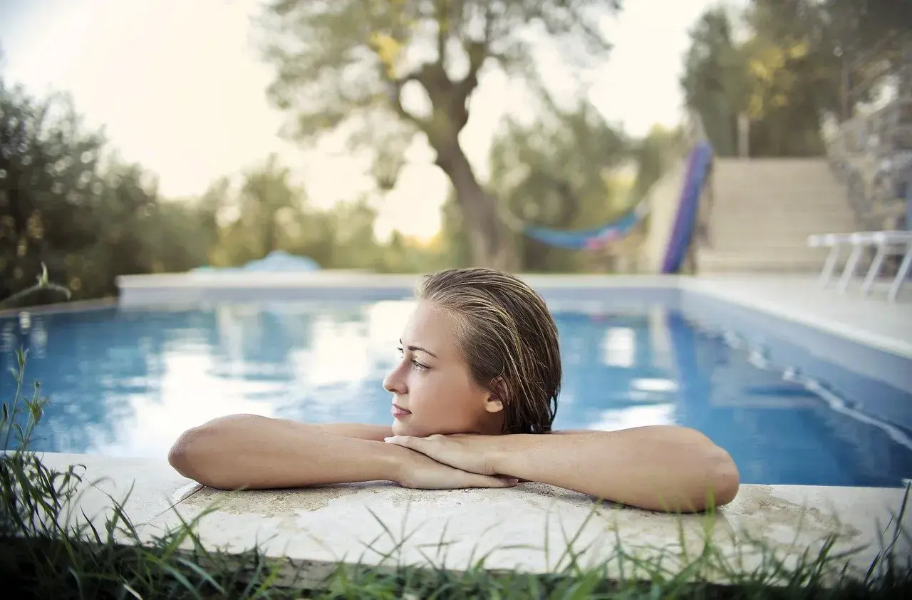 Jeune femme aux cheveux mouillés, profitant d'un moment de détente au bord de la piscine. L'eau bleue reflète le ciel, créant une ambiance paisible.