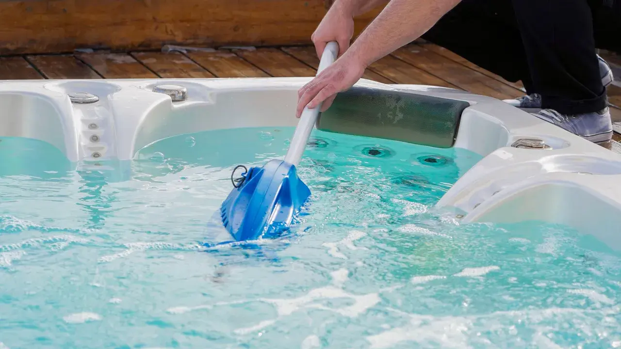 Nettoyage d'un spa en hiver avec un aspirateur manuel. L'eau est turquoise et des bulles se forment.