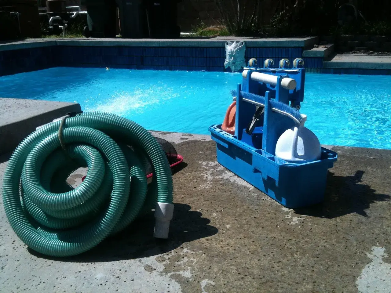 Kit d'entretien piscine pour les nuls : tuyau vert enroulé et boîte bleue avec accessoires de nettoyage.
