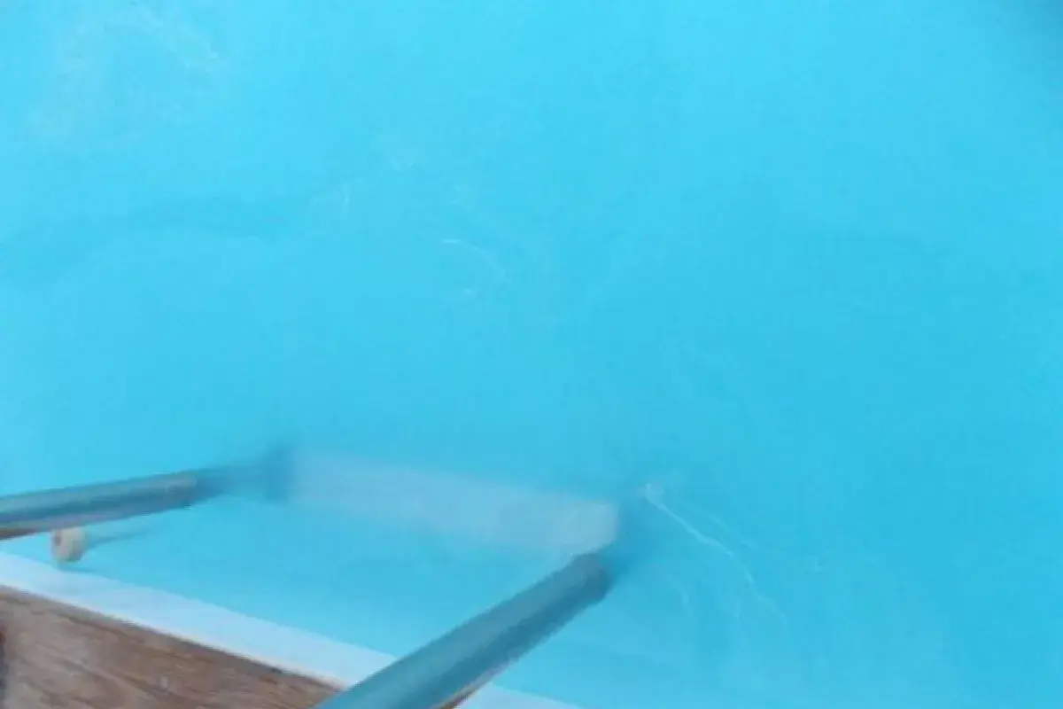 Nettoyage d'une piscine : un aspirateur sous-marin racle le fond, soulevant une eau trouble. Le sel dissous rend l'eau légèrement laiteuse.
