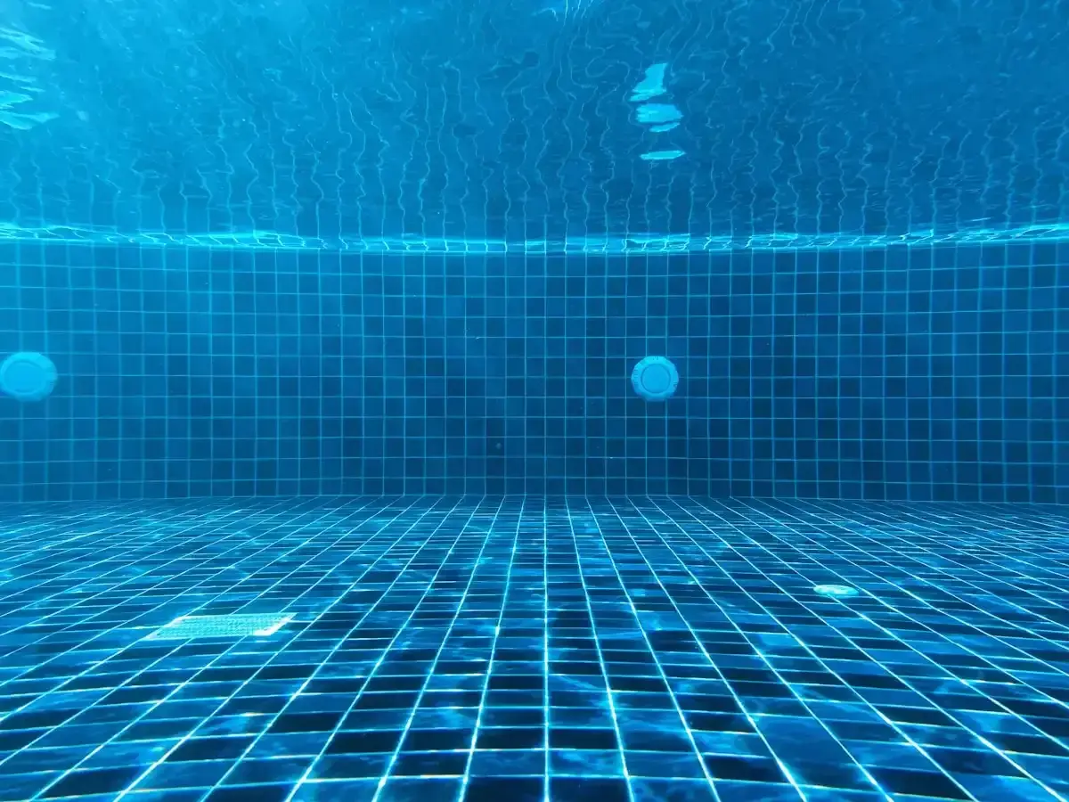 Vue sous-marine d'une piscine carrelée de bleu. La lumière du soleil filtre à travers l'eau. Question : chlore choc combien de temps faire tourner la pompe ?