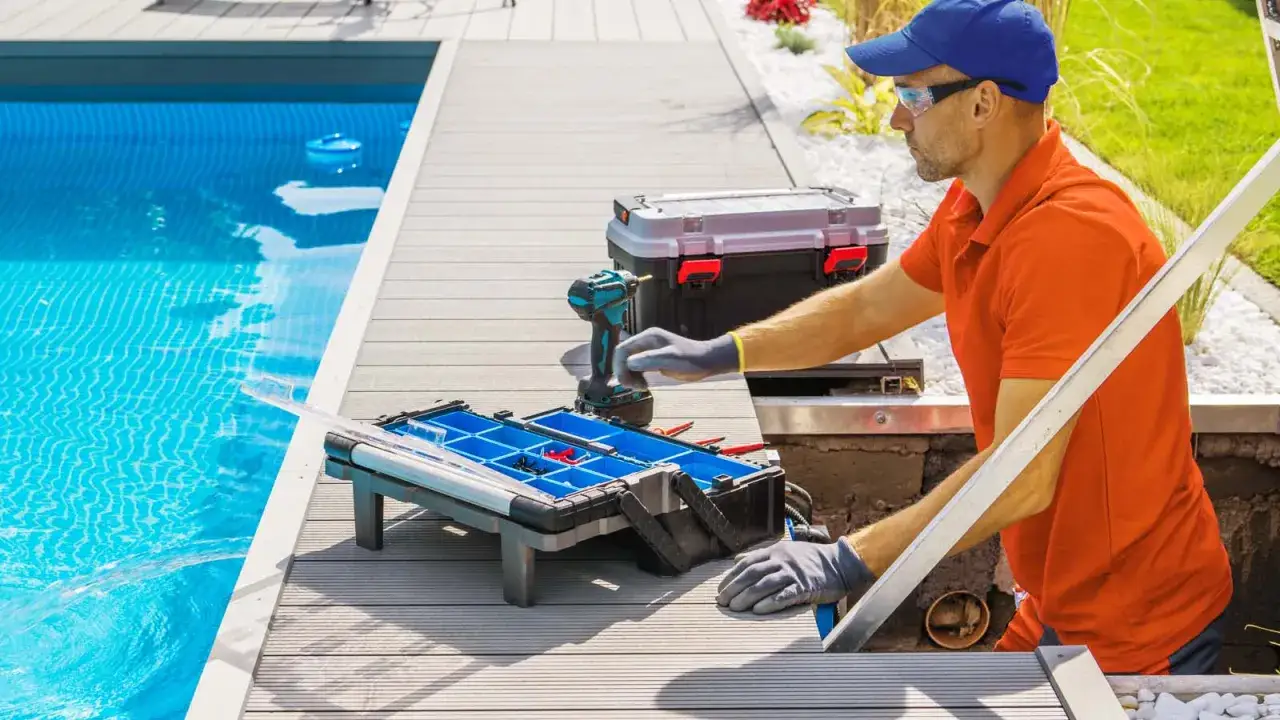 Un technicien répare une fuite de piscine. Il est près de l'eau bleue, avec une boîte à outils et une perceuse.