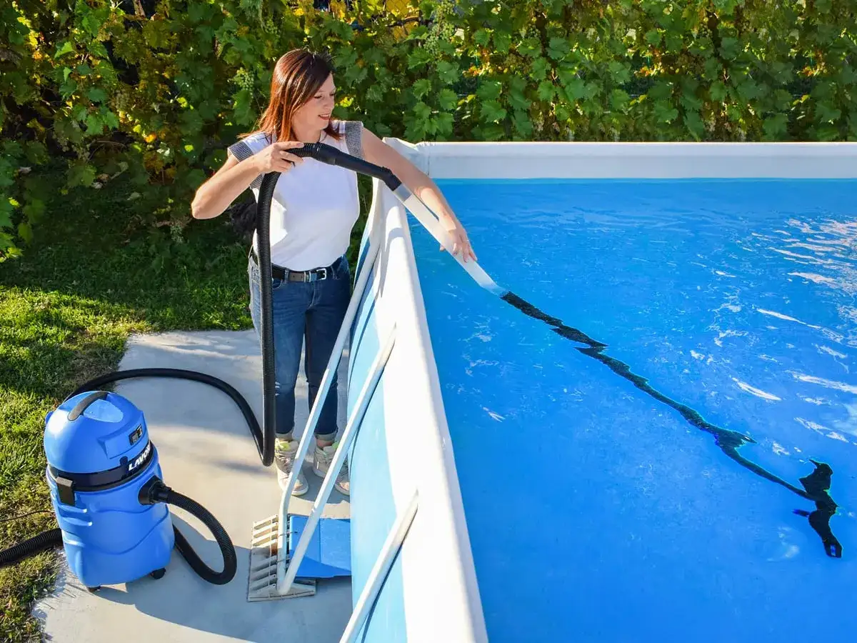 Femme utilisant un aspirateur pour la remise en route piscine après hivernage actif. L'eau est d'un bleu éclatant.