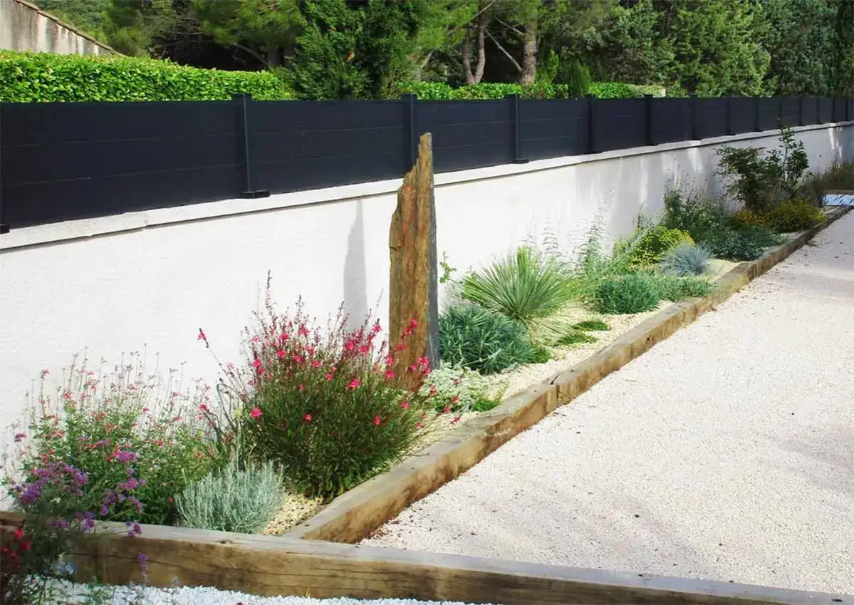 Jardin sec avec des plantes r&eacute;sistantes &agrave; la s&eacute;cheresse, des fleurs roses et un grand rocher vertical.