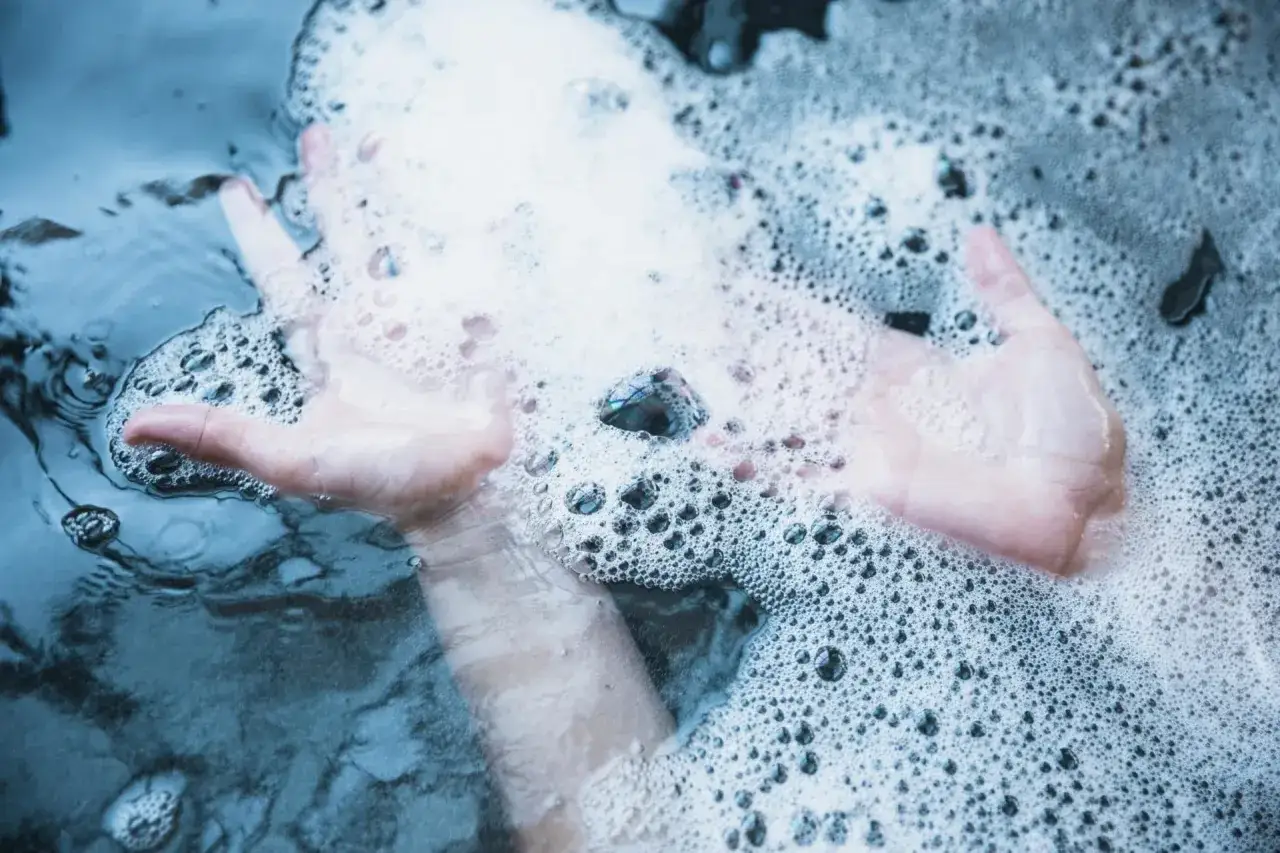 Mains douces dans un spa qui mousse, créant des bulles et des reflets apaisants.