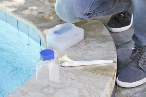 Test de piscine : une bouteille, un kit et une personne vérifient s'il y a trop de sel dans la piscine.