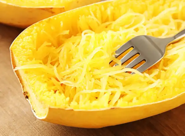 Une fourchette décompose les fils jaunes d'une courgette spaghetti cuite, prête à être dégustée.