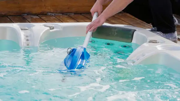 Nettoyage d'un spa en hiver avec un aspirateur manuel. L'eau est turquoise et des bulles se forment.