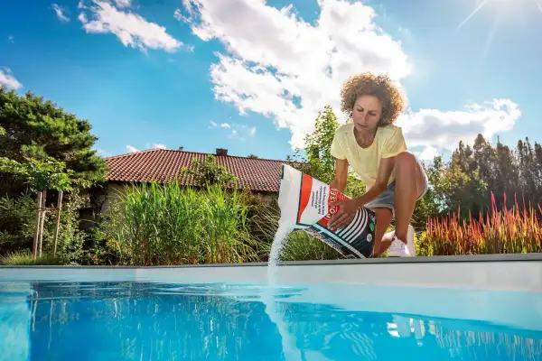 Femme versant du sel dans une piscine, assurant le bon temps de dissolution du sel pour une eau cristalline.
