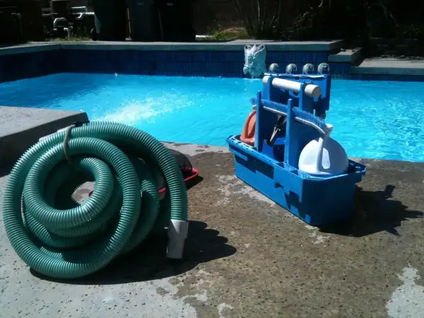 Kit d'entretien piscine pour les nuls : tuyau vert enroulé et boîte bleue avec accessoires de nettoyage.