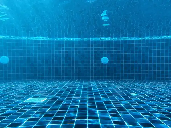 Vue sous-marine d'une piscine carrelée de bleu. La lumière du soleil filtre à travers l'eau. Question : chlore choc combien de temps faire tourner la pompe ?